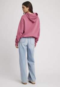 Un sweat à capuche rose à coupe décontractée, associé à un jean large bleu clair, doté de poches arrière et d'une texture délavée.