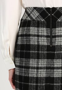 Jupe à carreaux noire et grise à taille haute, avec une fermeture éclair à l'avant et un tissu en laine doux et texturé. Design soigné.