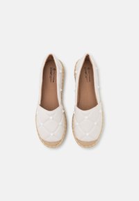 Chaussures blanches à enfiler matelassées avec des clous pointus et des semelles en jute tressé, vues du dessus sur un fond blanc.