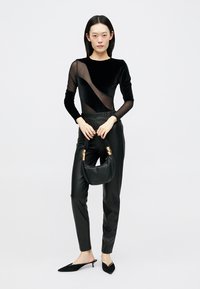 Black velvet bodysuit with sheer panels, high waist black leather pants, holding a soft black handbag with gold hardware, and black mules.