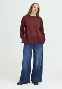 Pull en maille bordeaux avec un ourlet inférieur texturé, associé à un jean en denim bleu à jambes larges. Design simple avec des manches longues et une coupe décontractée.