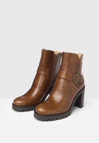 Bruine leren enkellaarsjes met een ronde neus, zijritsen, een riemdetail en een stevige zwarte hak. Gestructureerde buitenzool voor grip.