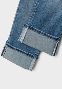 Blå denimbyxor med en ljusblå manschett. Har en rak passform, synlig söm och ett fransat nederkant. Standard denimtextur.