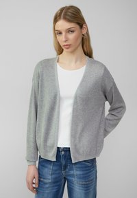 Hellgrauer Cardigan mit offenem Vorderteil, gerippten Bündchen und lockerer Passform, kombiniert mit einem weißen T-Shirt und blauen Jeans.