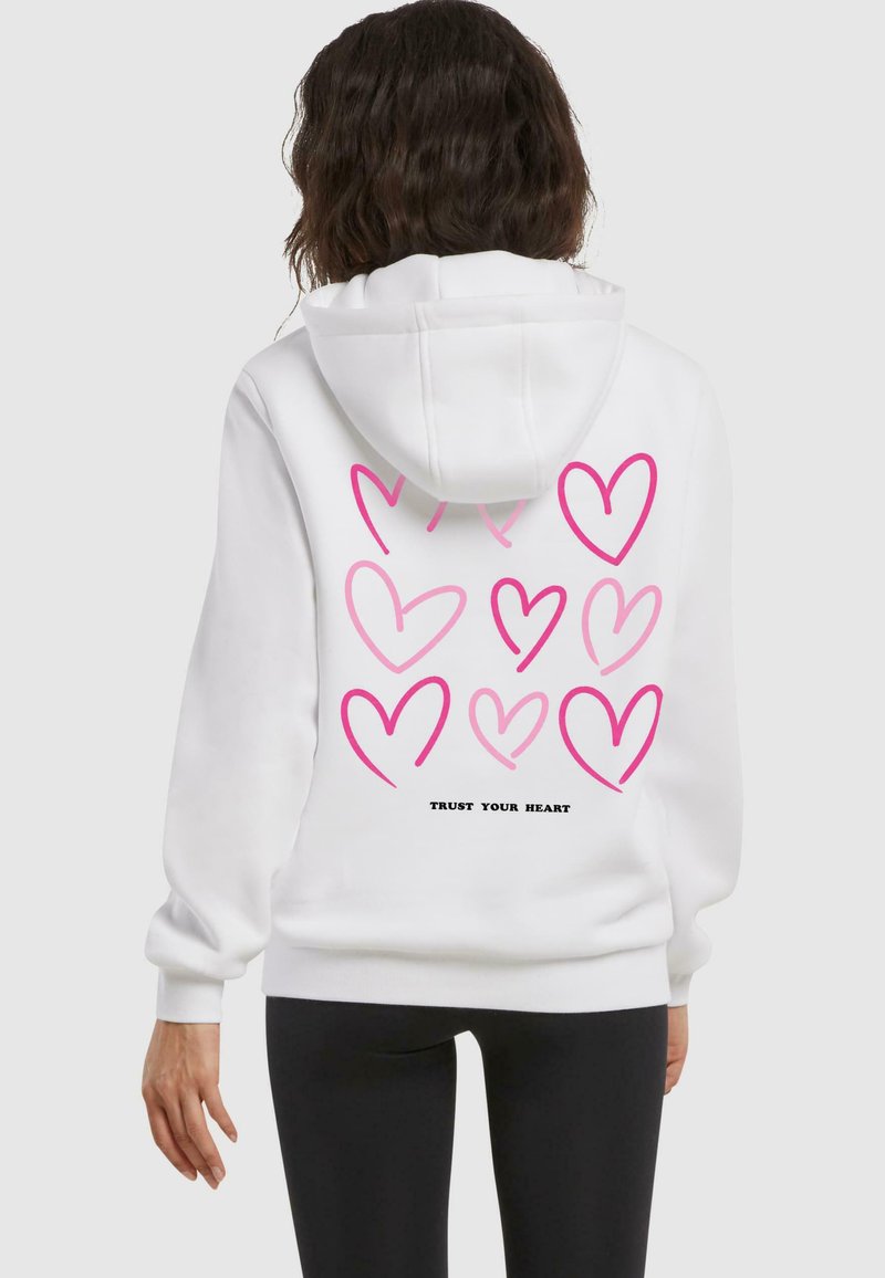 Felpa bianca con più cuori rosa sulla schiena e la scritta "FIDATI DEL TUO CUORE" in nero. Tessuto morbido, maniche lunghe e cappuccio.