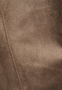 Bruin suede stof met een zichtbare zachte textuur en een verticale gestikte naad aan de linkerkant.