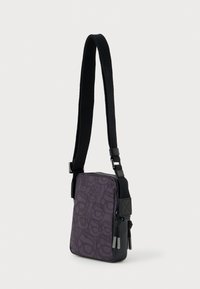 Mažas juodas per petį nešiojamas krepšys su raštuotu priekiu, reguliuojama petneša ir užtrauktukų uždarymai su metaliniais trauklapiais.