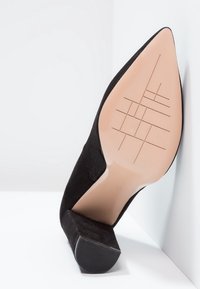 Bottine en daim noir à bout pointu avec talon bloc, montrant la semelle avec un motif de crampons croisés et la taille 37 indiquée.