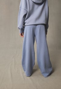 Sweat-shirt en coton bleu clair avec capuche, associé à un pantalon de survêtement large assorti, présentant une texture douce et une coupe décontractée.