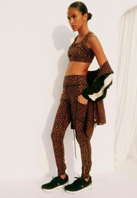 Leopard print sportoutfitset met een sportbeha en high-waisted leggings, aangevuld met een zwarte jas met witte accenten.