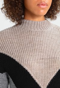 Strickpullover mit hohem Kragen, Farbblockdesign in Beige, Grau und Schwarz sowie einer strukturierten, gerippten Oberfläche.