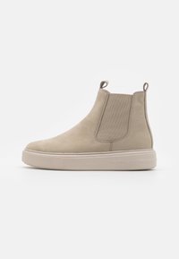Beige Wildleder-Ankle-Boot mit elastischen Seiteneinsätzen, Ziehlasche und dickem Plateausohlen, der eine glatte Textur und ein minimalistisches Design aufweist.