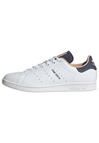 Valge nahast tossud sinise kanna detailiga, auguliste küljeelementidega, "STAN SMITH" brändinguga ja valge kummist tallaga. Klassikaline disain, madala vormiga stiil.