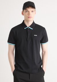 Czarna koszulka polo z kołnierzykiem wykończonym turkusowym akcentem, z dwoma guzikami przy dekolcie oraz małym białym logo na piersi.