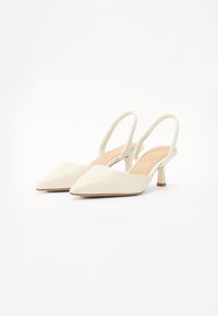 Valged slingback kontsad, millel on terav varvas, madal silindriline konts, sile viimistlus ja minimalistlik disain. Rõhutatud beezide siseosadega.