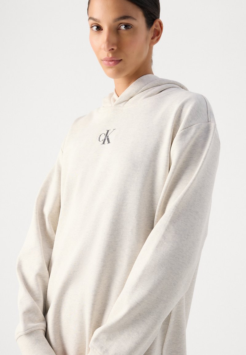 Lichtbeige hoodie van zacht materiaal, met een buideltas aan de voorkant en een klein logo op de borst. Lange mouwen met gefronste manchetten.