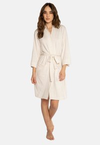 Robe di colore beige chiaro, lunga fino al ginocchio, realizzata in un tessuto morbido. Presenta un design avvolgente, chiusura con cravatta e due tasche frontali. Maniche lunghe con una vestibilità comoda.
