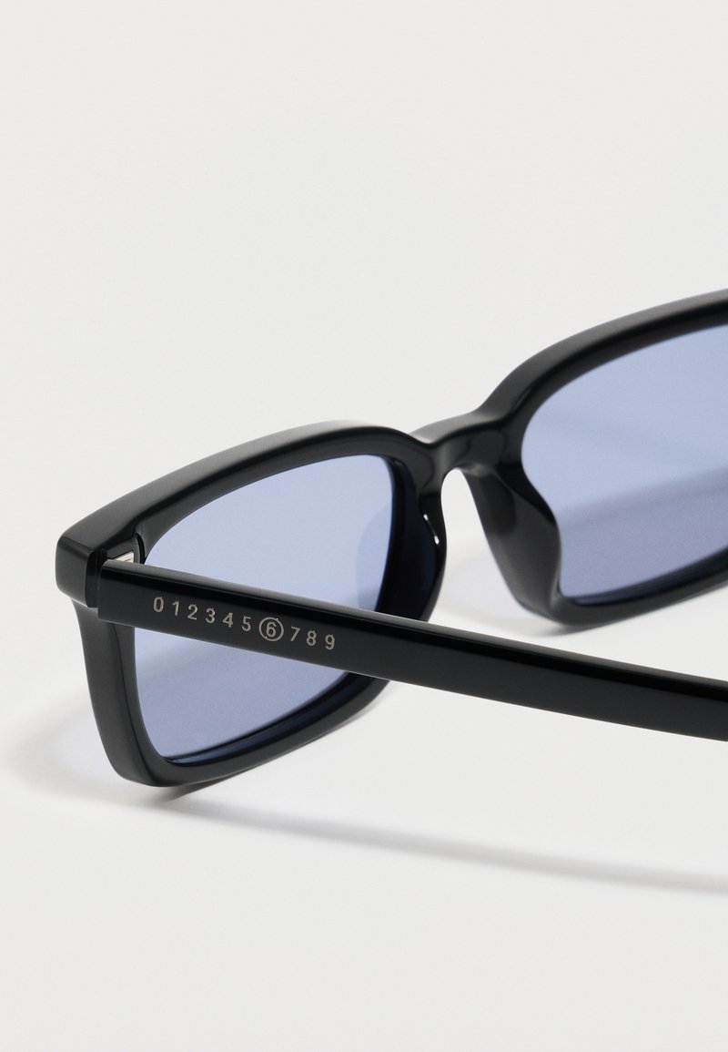 Lunettes de soleil rectangulaires noires avec verres teintés bleus et marquage numérique sur la branche allant de 0 à 9 avec le chiffre 6 entouré.