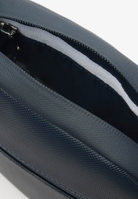 Tamnoplavi ženski ručni torbica s teksturiranom vanjštinom i zatvaranjem na patentni zatvarač, s glatkim unutrašnjim oblogom. Kompaktni dizajn s elegantnim siluetom.