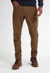 Bruine corduroy broeken met een rechte pasvorm, voorzien van subtiele verticale ribbels, zijzakken en een ritssluiting. Gecombineerd met bruine veterlaarzen.