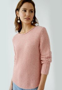 Helle rosa Strickpullover mit gerippter Textur, Rundhalsausschnitt und geknöpften Ärmeln, kombiniert mit hellblauen Jeans.