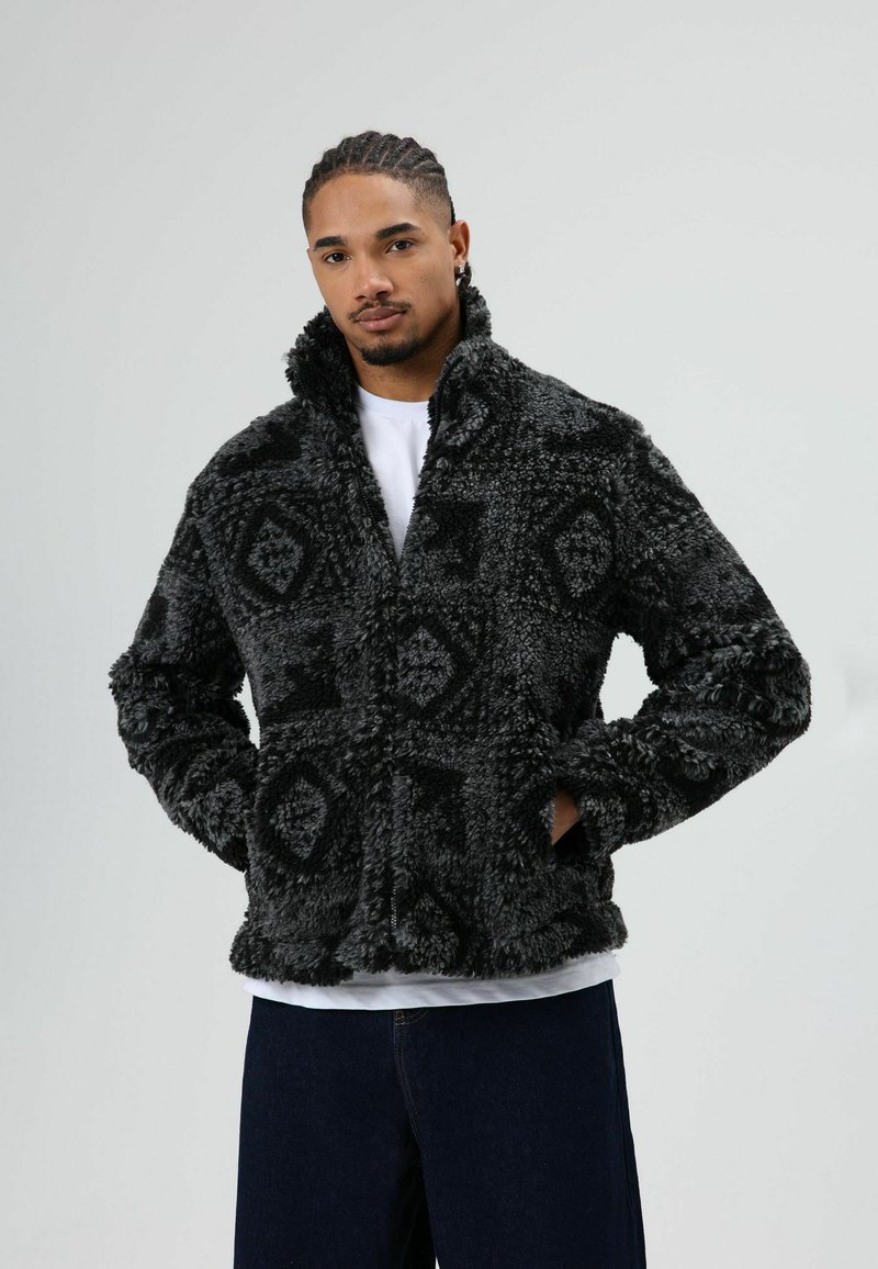 Zwart-grijze, pluizige jas gemaakt van gestructureerde stof, met een geometrisch patroon, hoge kraag en voorzakken.