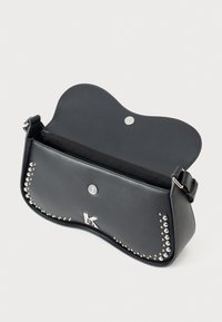 Bolsa de ombro em couro preto com tachas prateadas ao longo das bordas, um emblema prateado com a letra "K" e uma aba com fecho magnético.