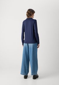 Mornarska dugosleeve majica u kombinaciji sa širokim plavim trapericama, koje imaju glatku teksturu i opušten kroj. Crne platforme upotpunjuju izgled.