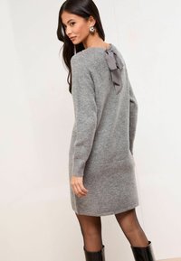 Rochie tricotată gri cu mâneci lungi, având un detaliu sub formă de fundiță la gâtul din spate. Textură netedă și siluetă ușor ajustată.