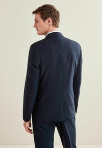 Chaqueta de traje azul marino hecha de una tela suave, con un corte entallado, detalles de costura sutiles y una abertura sencilla en la parte posterior, con puños abotonados.