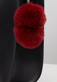 Mustapohjainen nahkalaukku, jossa on kaksi punaista keinoturkista pom-pom-palloa. Silkkinen pinta, johon on kiinnitetty pyöreät pom-pomit hopeisen metallilenkin avulla.