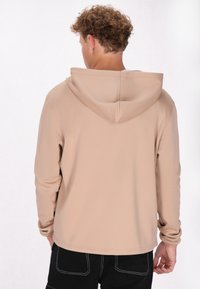 Beige hoodie met een gladde textuur, lange mouwen en een ontspannen pasvorm. Geen zichtbare patronen of hardware-details.