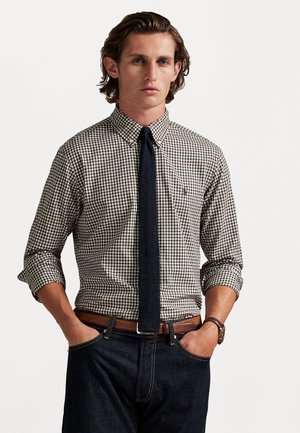 Bruin en wit geruit shirt met soortkraag, gecombineerd met een donkere gestructureerde stropdas en donkere jeans. Bruin leren riem en horloge details.