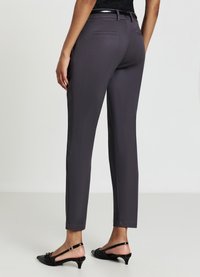 Pantalon ajusté, gris foncé, avec une texture lisse. Présente une simple poche arrière et une ceinture noire lisse et brillante. Porté avec des talons ouverts noirs.