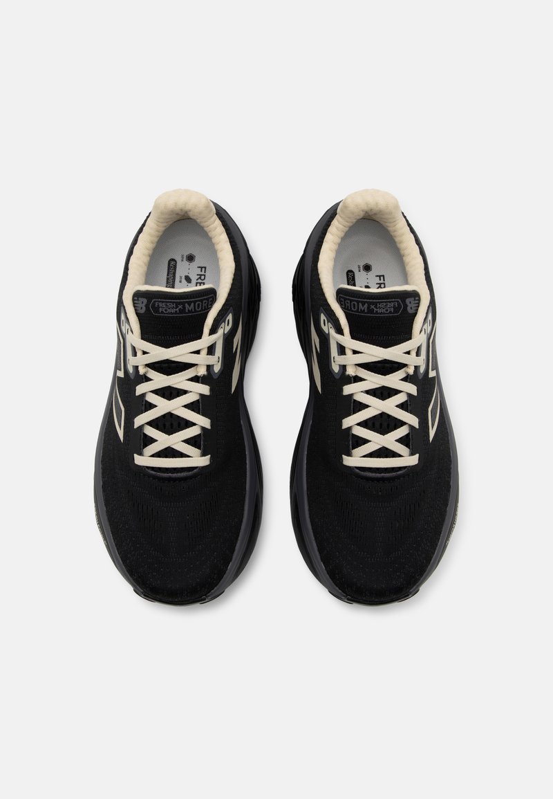 Zapatillas deportivas negras con parte superior de malla, cordones crema, cuello acolchado y detalle del logo en contraste en el costado. Suela plana con agarre texturizado.