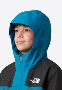 Blauw-zwart capuchonjack met een ritssluiting aan de voorkant, voorzien van een logo op de borst en een gestructureerde stof, geschikt voor koud weer.