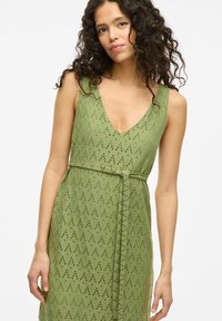 Grünes ärmelloses Kleid mit V-Ausschnitt, strukturiertem Stoff mit Lochmuster und einem gebundenen Taillengürtel.