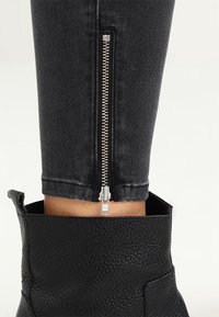 Närbild av svarta denimbyxor med silverdragkedja ovanför svarta texturerade läderstövlar.