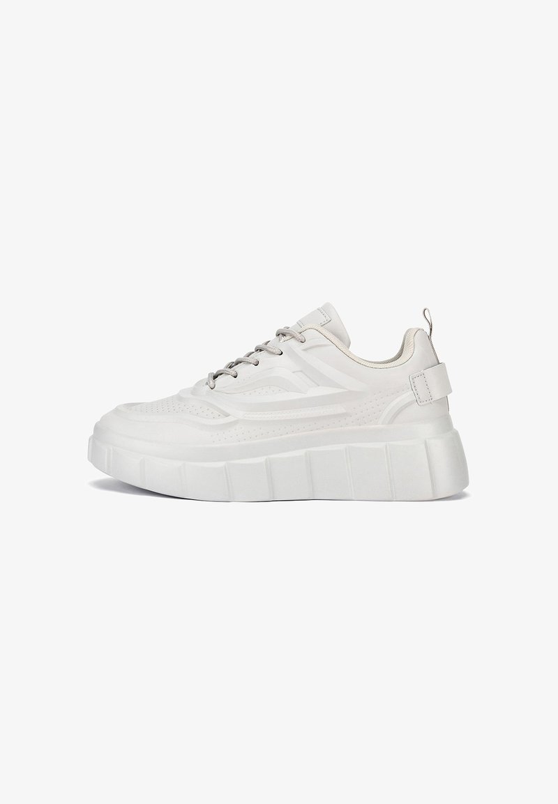 Zapatilla blanca con parte superior texturizada, presenta perforaciones, una suela gruesa y detalles metálicos en los cordones y la lengüeta del talón.