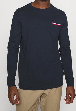 Mörkblå långärmad t-shirt i bomull med en bröstficka som har röd, vit och blå rand. Rundad hals med åtsittande ärmar.