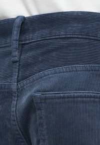 Sötétkék kordbársony nadrág, függőleges bordázott mintázattal, varrott derékpánttal és hátsó zseb részletekkel.