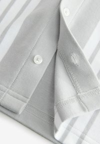 Gros plan d’un tissu rayé gris et blanc avec un bouton et des détails de boutonnière sur un bord de vêtement plié.