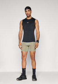 Must varrukateta sportlik topp valge logoga, oliivrohelised sobivad lühikesed püksid, mustad spordijalatsid ning sobivad mustad peapael ja randmepael.