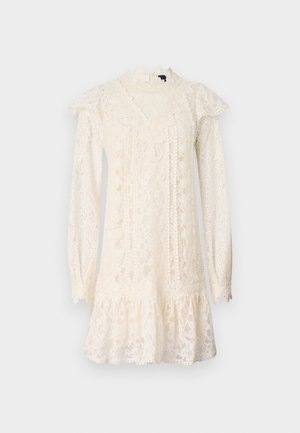 Lace dress in ivory with long sleeves, high neck, ruffled accents, and a tiered hem. Features intricate floral patterns throughout.