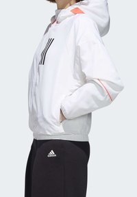 Hvid hættejakke med en glat overflade, der har et sort stribet design på fronten og en koralfarvet detalje på skuldrene.