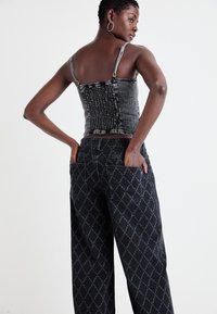 Črn denim crop top z teksturiranimi paneli in tankimi naramnicami, v kombinaciji s črnimi širokimi hlačami z vzorcem, ki vsebujejo diamante in velike žepi.