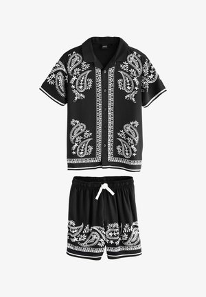 Schwarzes kurzärmliges Hemd mit Knöpfen und Shorts mit weißen Paisley- und Blumenmustern, elastischer Bund an den Shorts mit weißem Kordelzug.