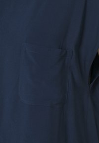Camicia a maniche corte blu navy con tasca sul lato sinistro, realizzata in tessuto liscio con una leggera lucentezza e dettagli di cucitura puliti.