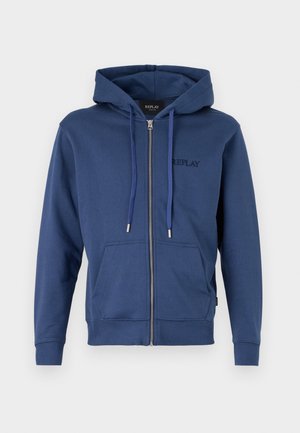 Hoodie zippé bleu marine avec une poche avant, une capuche avec cordon de serrage, des poignets côtelés et un logo brodé discret sur la poitrine. Matériau doux.