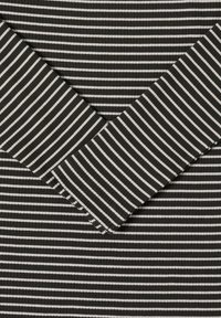 Czarno-biała tkanina w paski o prążkowanej fakturze, z naprzemiennie szerokimi i wąskimi paskami. Dwa rękawy zachodzą na siebie po przekątnej.